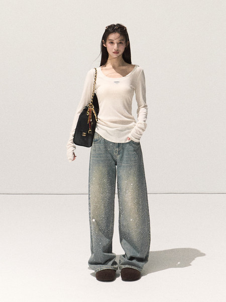 Model wearing a white long-sleeve top with sparkly wide-leg jeans and a black shoulder bag