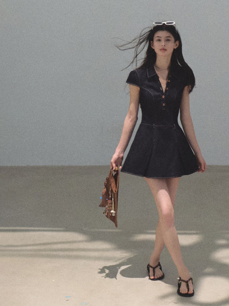 Model wearing a black short-sleeve mini dress with sandals and a small handbag