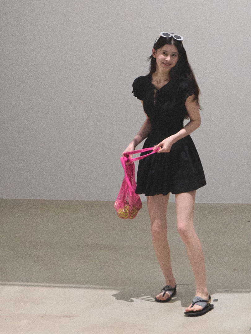 Woman wearing a black short dress and sandals while holding a pink mesh bag