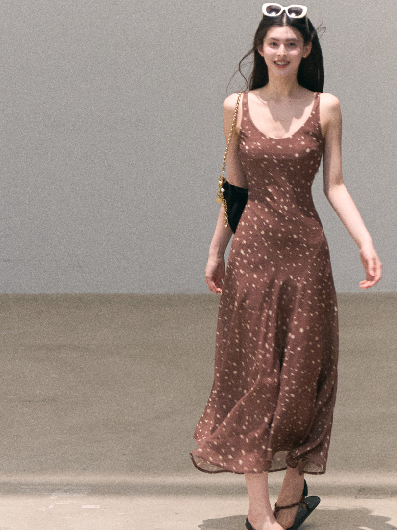 Model wearing a brown speckled sleeveless midi dress with a chain-strap bag