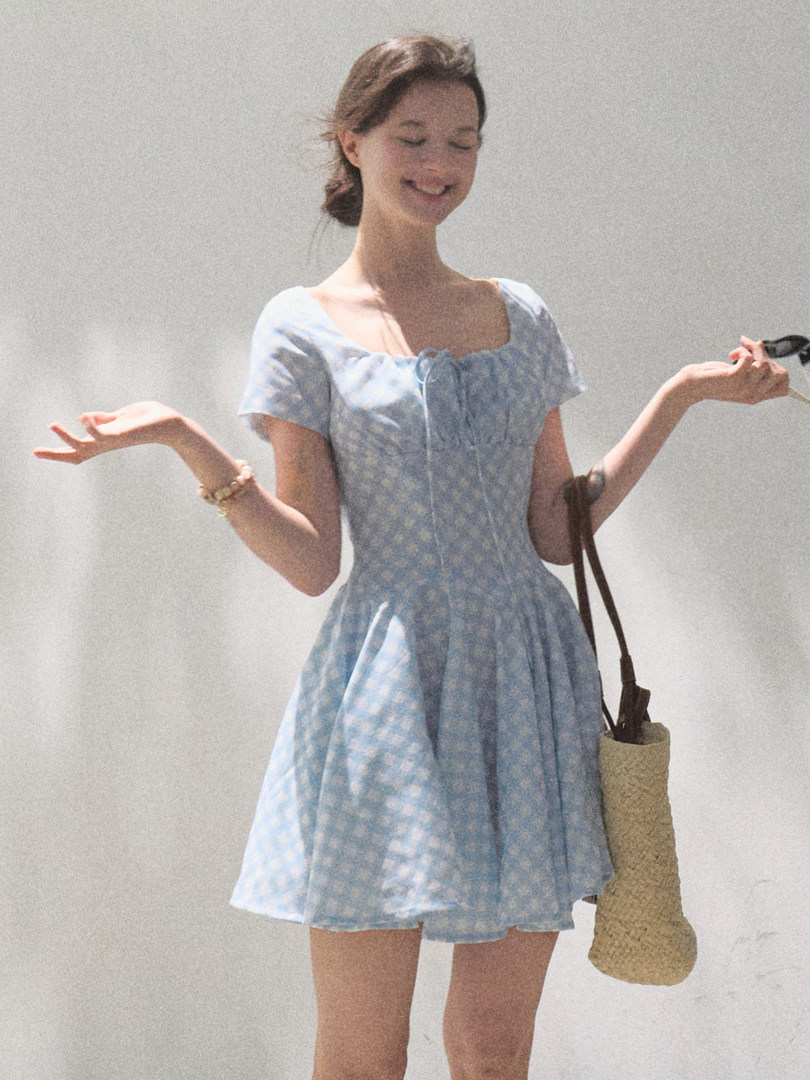Woman wearing a light blue floral mini dress and holding a woven bag