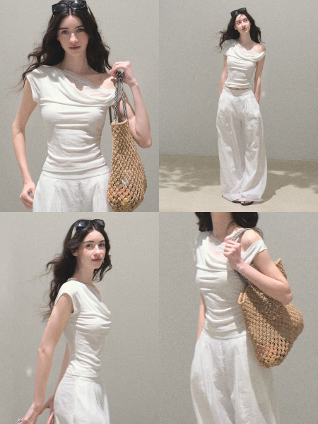 Woman modeling a white off-shoulder top and wide-leg pants with a woven tote bag