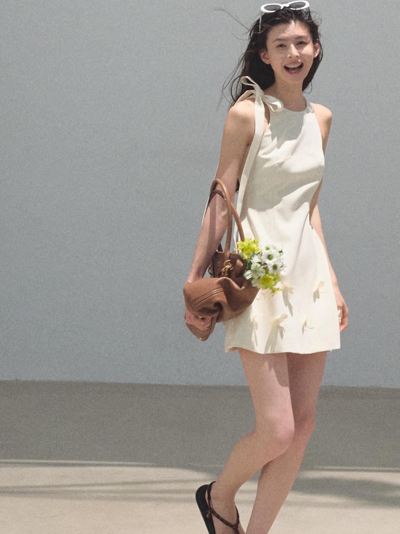 Woman wearing a white sleeveless mini dress with a brown shoulder bag