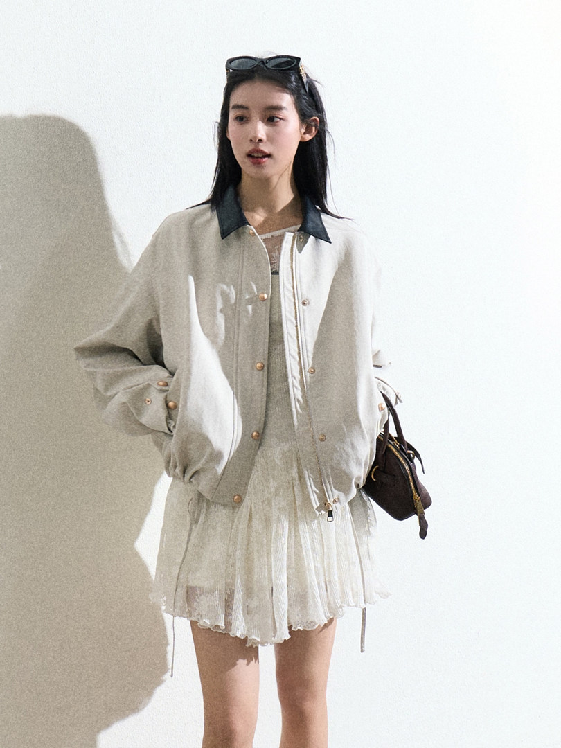 Model wearing a light bomber jacket over a sheer dress with a small handbag