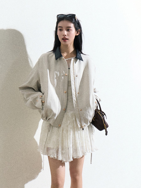 Model wearing a light bomber jacket over a sheer dress with a small handbag