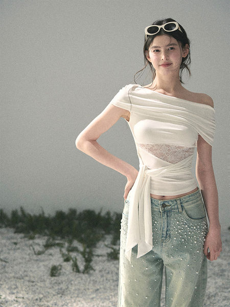 Woman modeling a white off-shoulder wrap top with embellished light-wash jeans