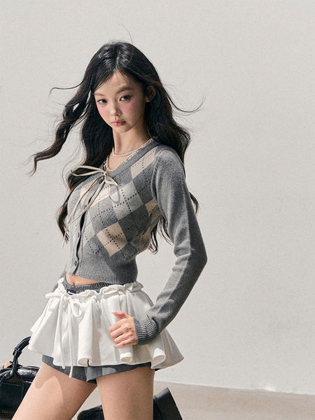 Model wearing a gray argyle cardigan with a white ruffled mini skirt over shorts