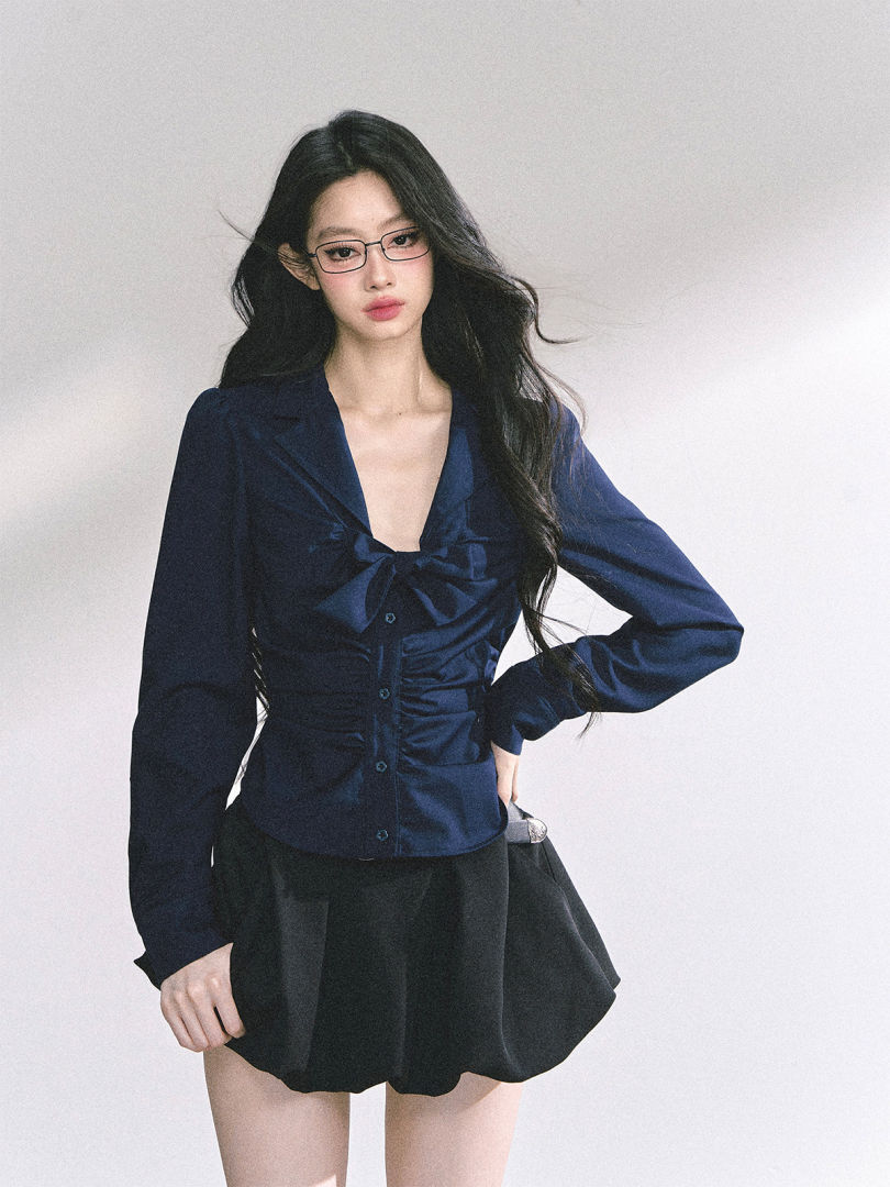 Model wearing a navy long-sleeve blouse with a bow detail and a black mini skirt