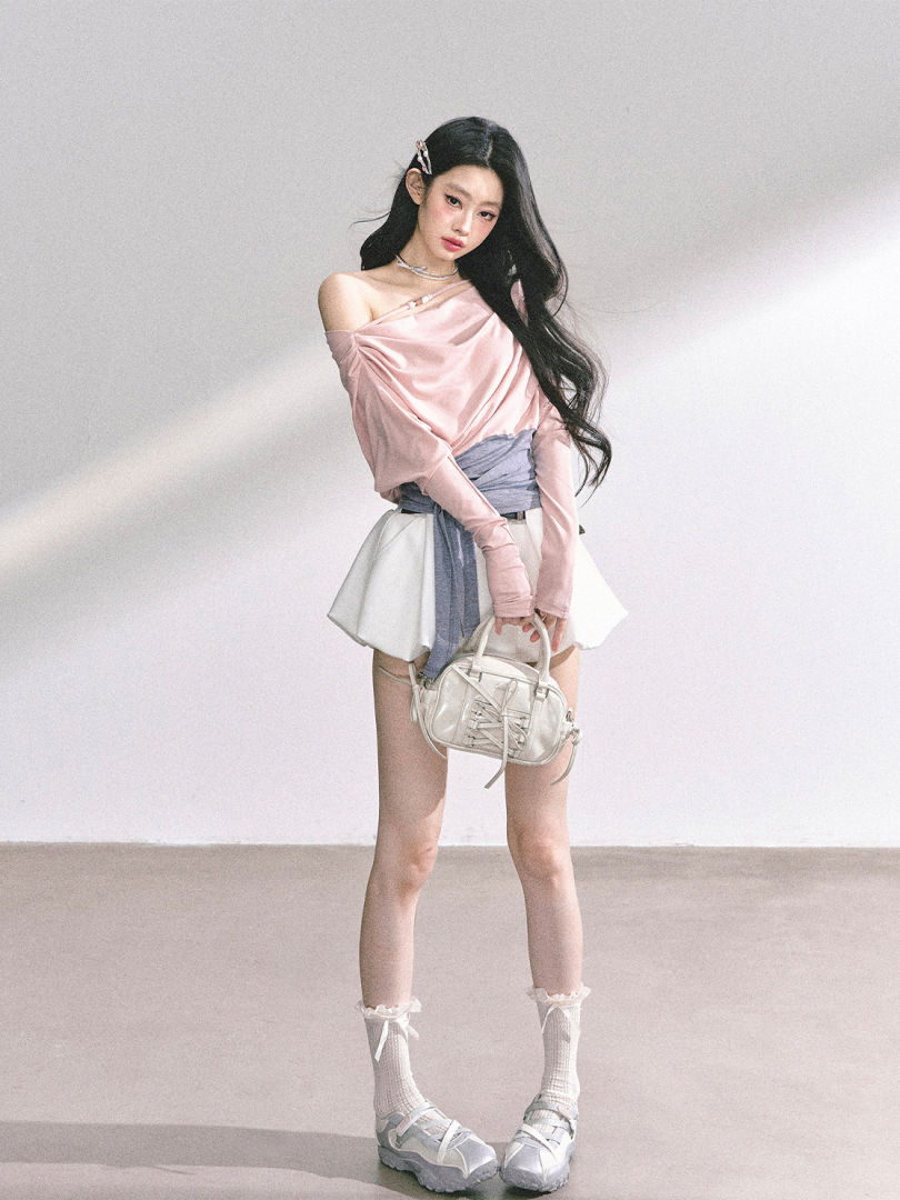 Woman wearing a pastel pink off-shoulder top, white mini skirt, and small white handbag