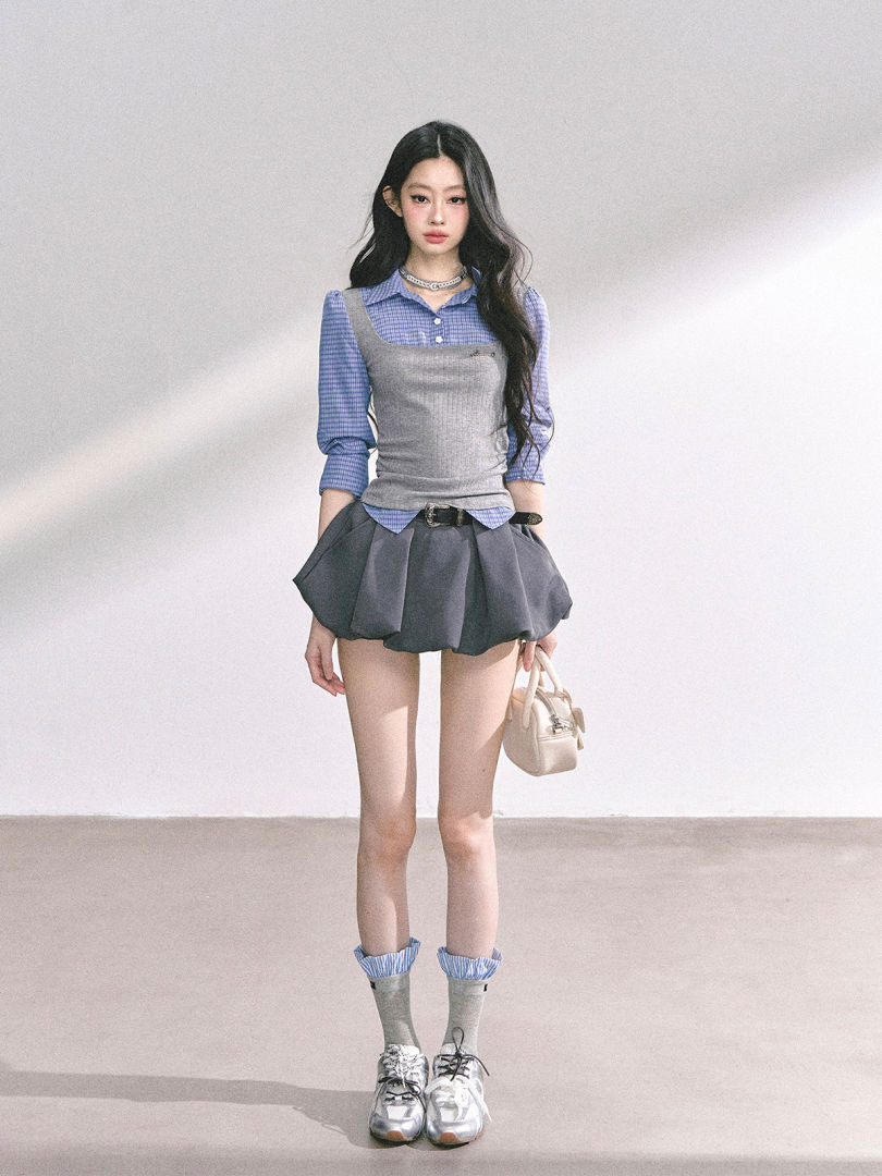 Fashion model wearing a blue plaid shirt with a gray corset top, pleated mini skirt, and sneakers