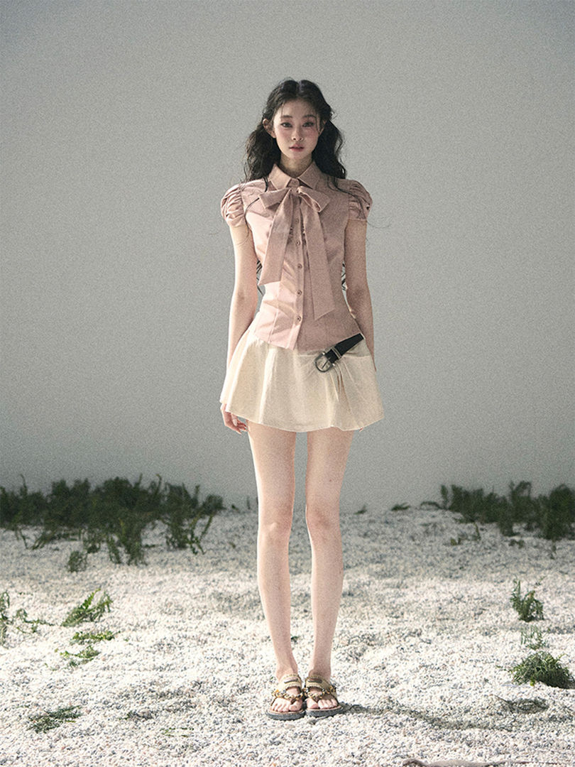 Model wearing a pink bow blouse with a cream mini skirt and sandals