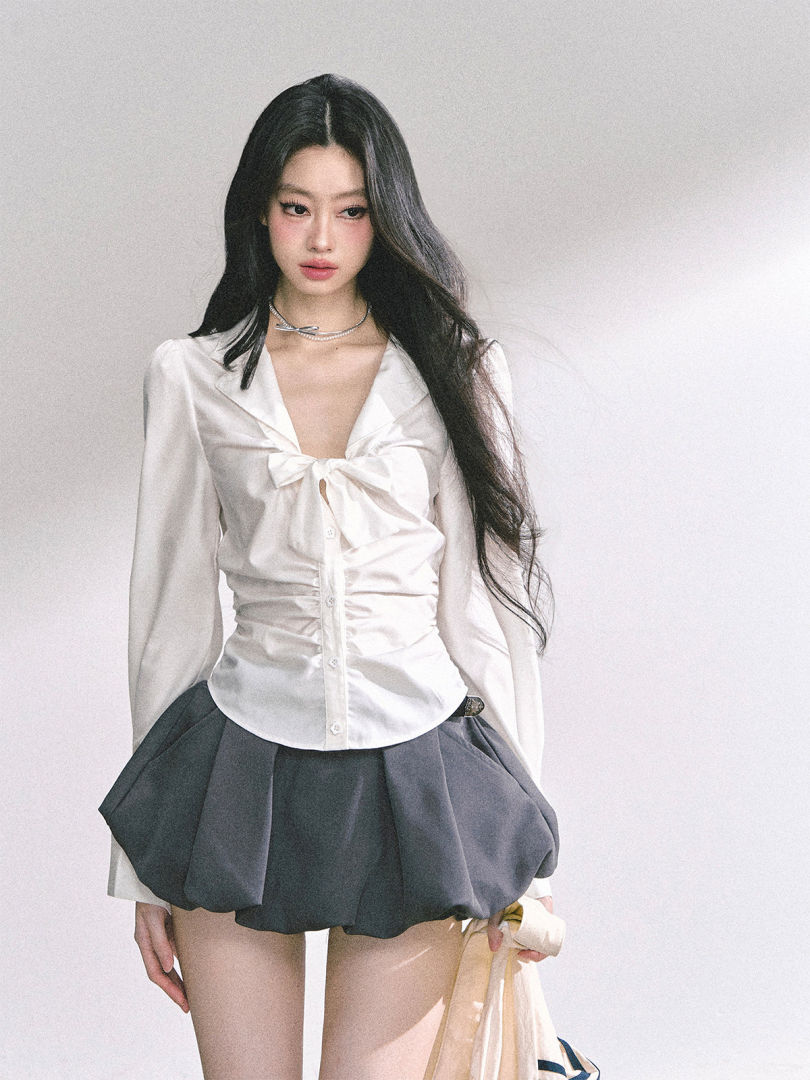 Model wearing a white ruched blouse with a dark puff mini skirt