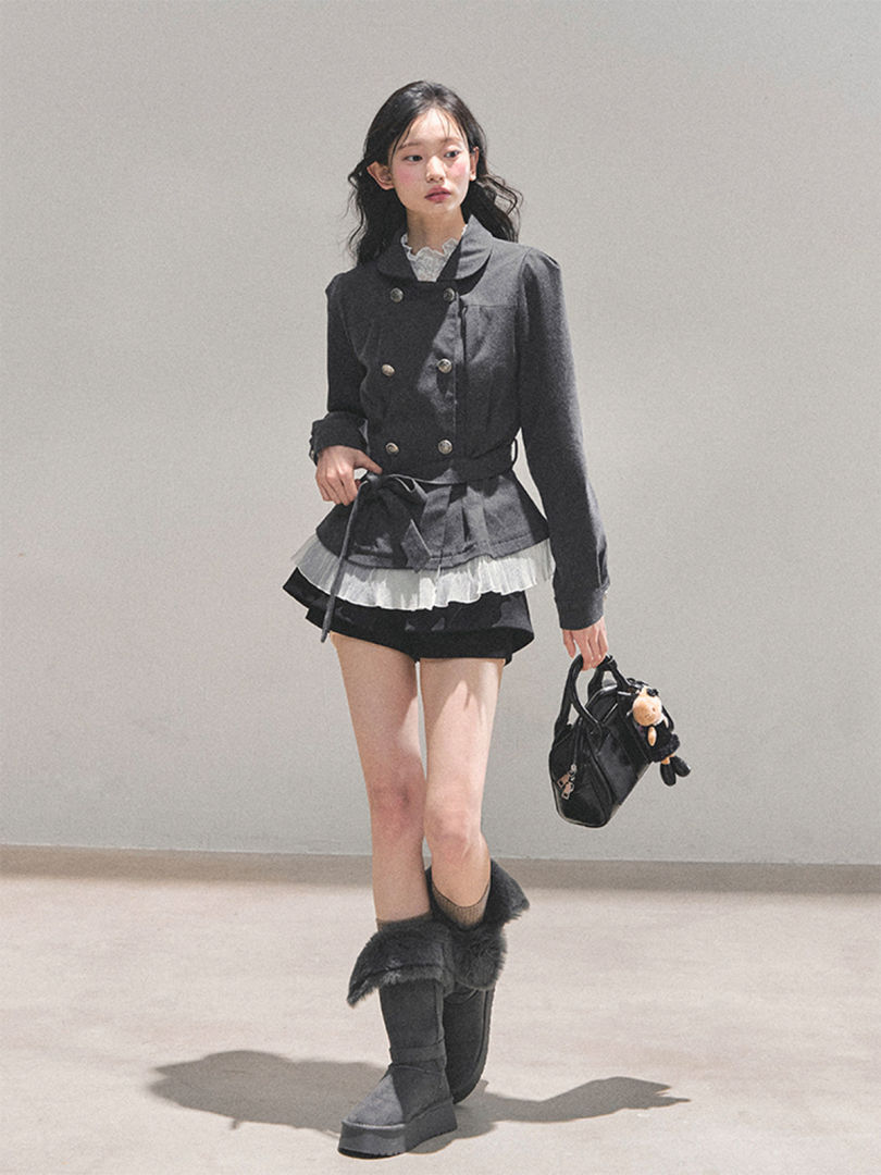 Model wearing a dark double-breasted jacket, layered skirt, and fur-trimmed boots