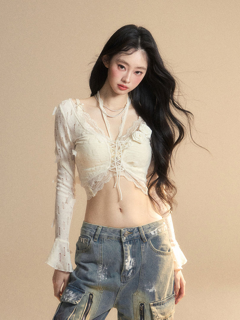 Model wearing a white lace long-sleeve crop top with distressed wide-leg denim pants