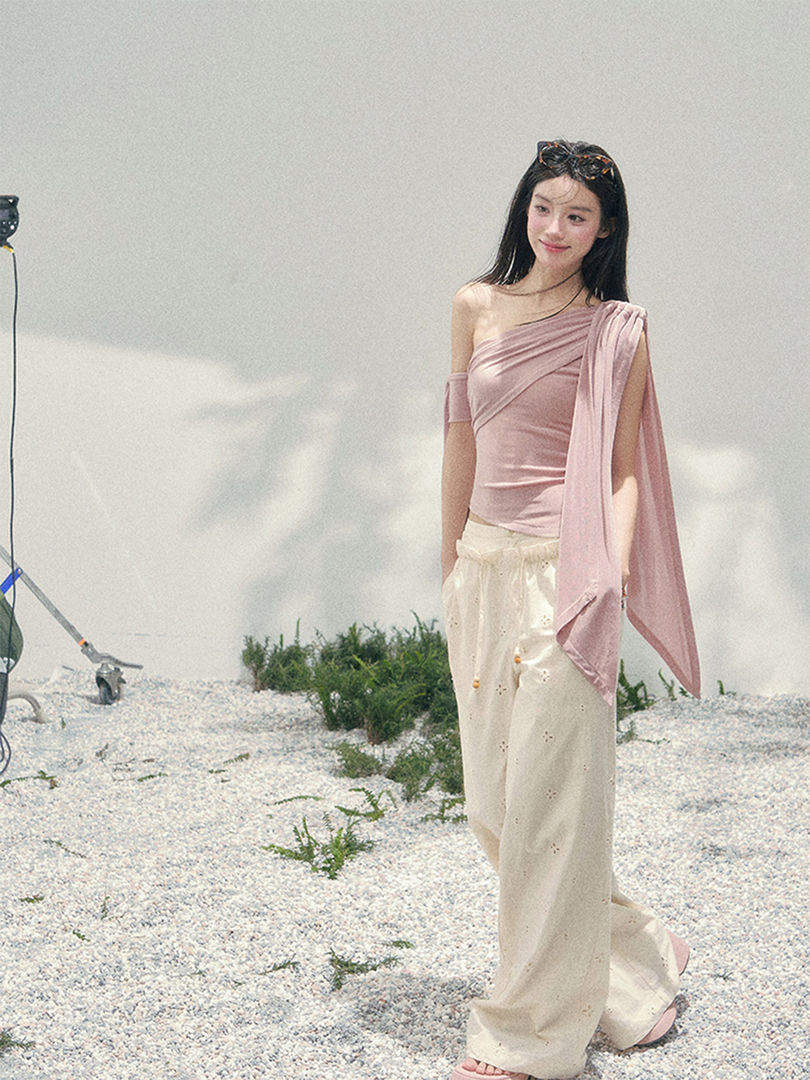 Model wearing a pink asymmetrical off-shoulder top with cream wide-leg pants