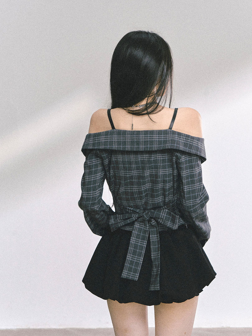 Woman wearing a dark plaid off-shoulder long-sleeve top with a tied back detail