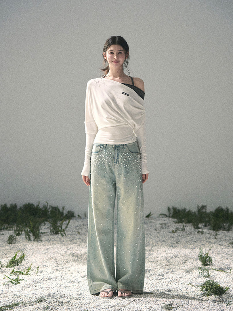 Model wearing a white off-shoulder top and embellished wide-leg jeans on a beach setting