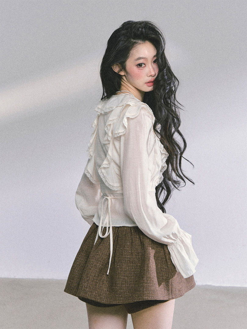 Woman modeling a sheer white ruffled blouse with a brown plaid skirt