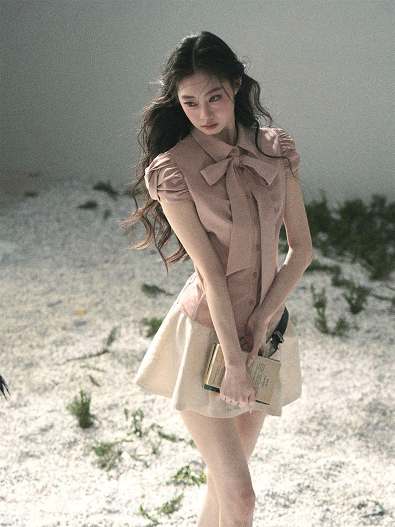 Model wearing a light pink bow blouse with a cream mini skirt outdoors