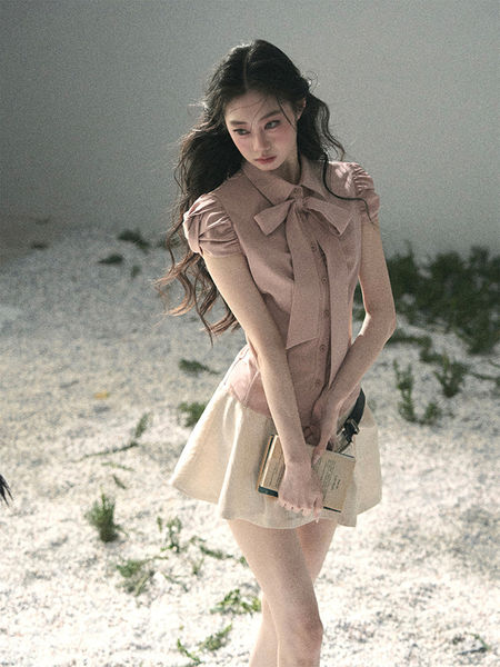 Model wearing a light pink bow blouse with a cream mini skirt outdoors