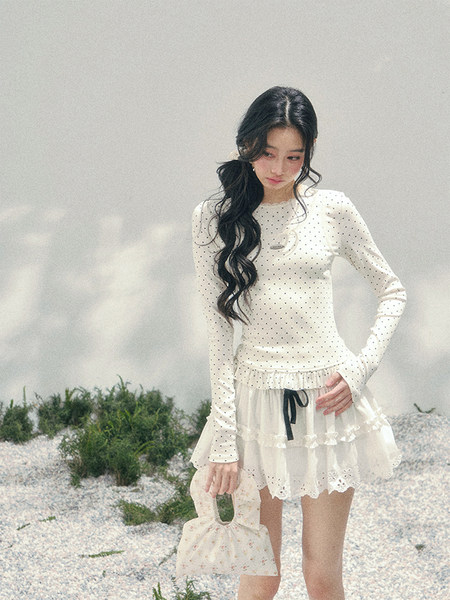 Model wearing a white polka dot long-sleeve top with a layered skirt and matching handbag