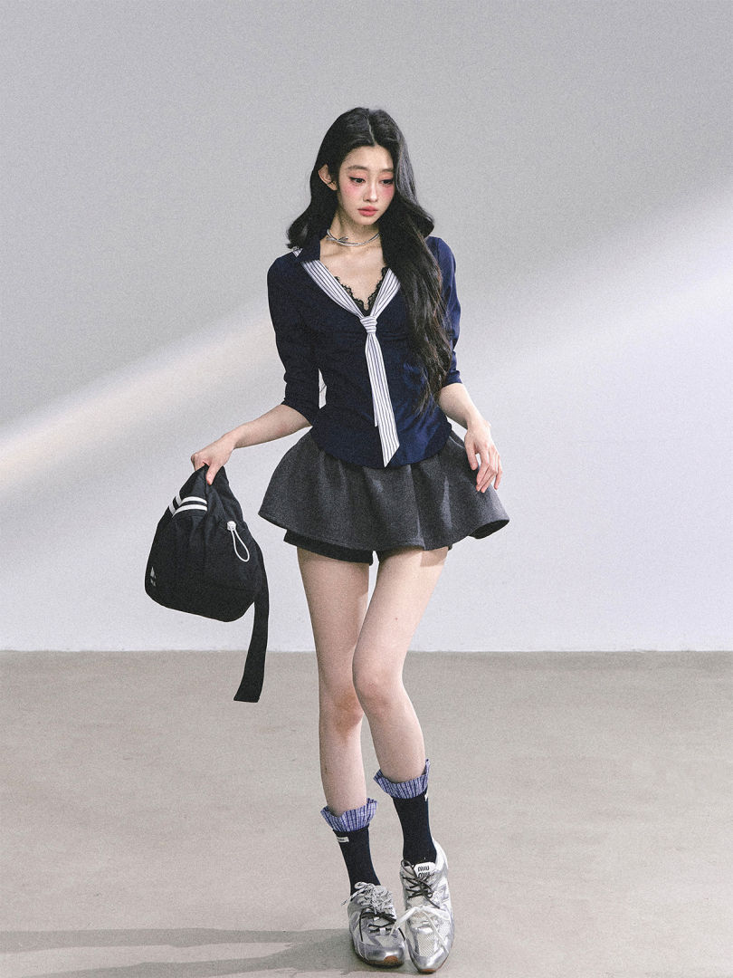 Model wearing a navy sailor-style top with a gray mini skirt, socks, sneakers, and a black bag.