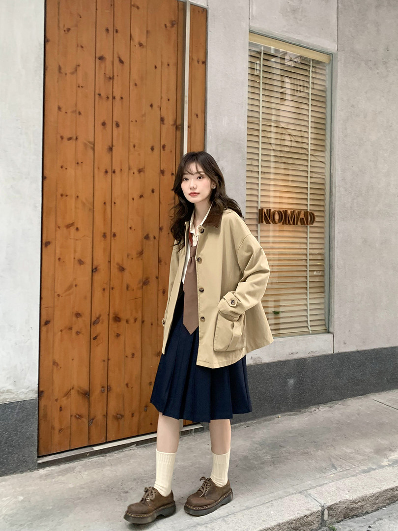Woman wearing a beige jacket with a navy skirt and brown shoes outdoors