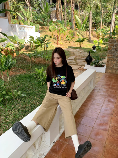 Model wearing a black graphic T-shirt and beige wide-leg pants outdoors