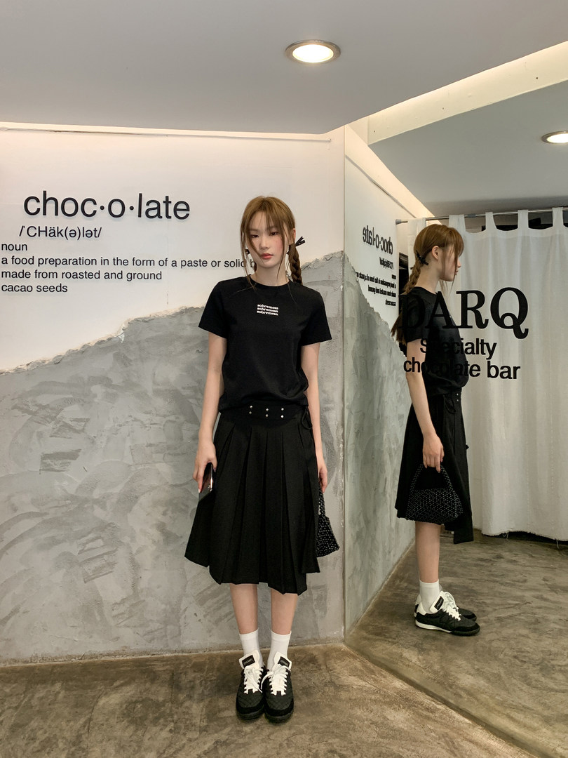 Woman modeling a black T-shirt and pleated skirt outfit with sneakers