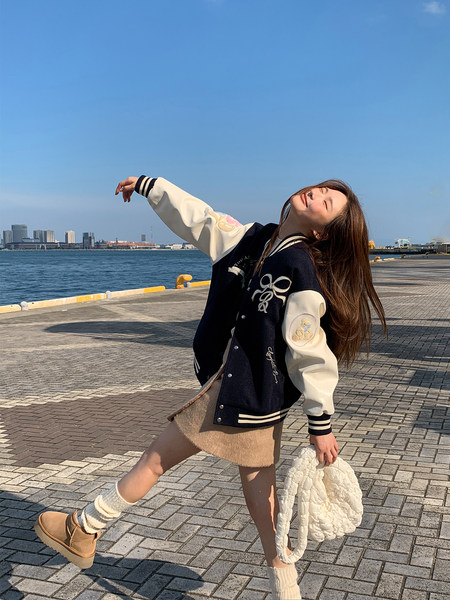 Woman wearing a black-and-cream varsity jacket with a quilted white handbag outdoors
