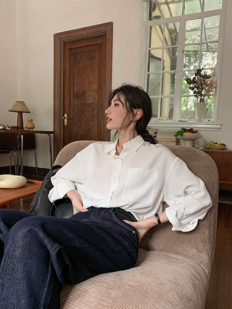 Woman wearing a white button-up shirt and dark jeans seated in a chair