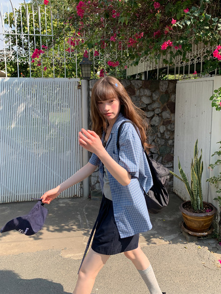 Model wearing a blue plaid short-sleeve shirt with black shorts outdoors