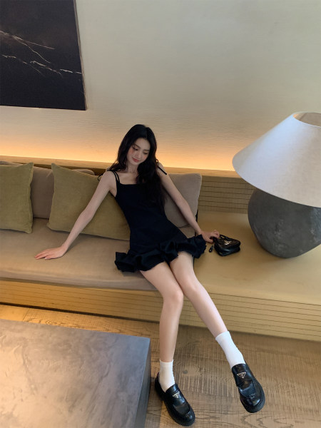 Woman wearing a black strappy ruffle mini dress with black loafers and white socks
