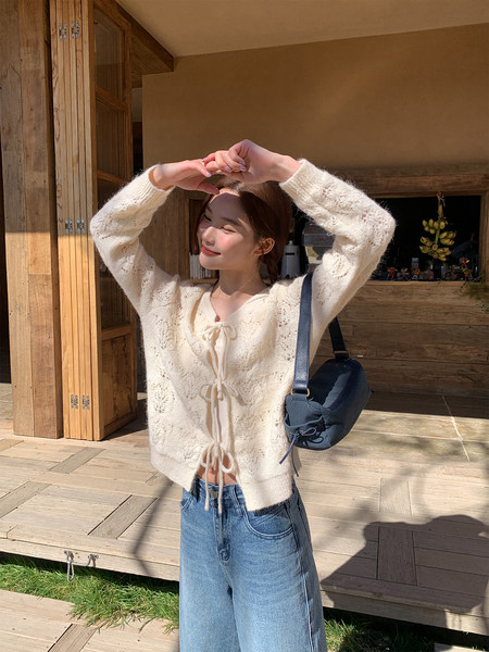 Woman wearing an ivory lace-up knit cardigan and blue jeans outdoors