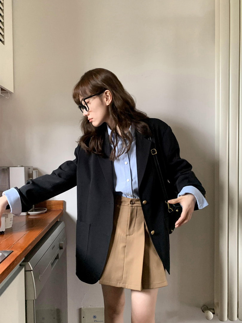 Woman wearing a black blazer over a light blue shirt with a beige skirt
