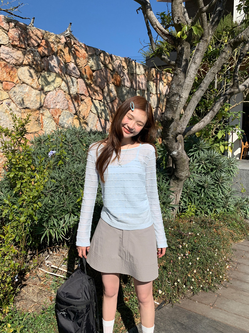 Woman wearing a light blue long-sleeve top with a beige mini skirt outdoors