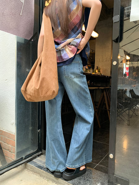 Woman wearing wide-leg jeans and a colorful sleeveless top with a tan tote bag