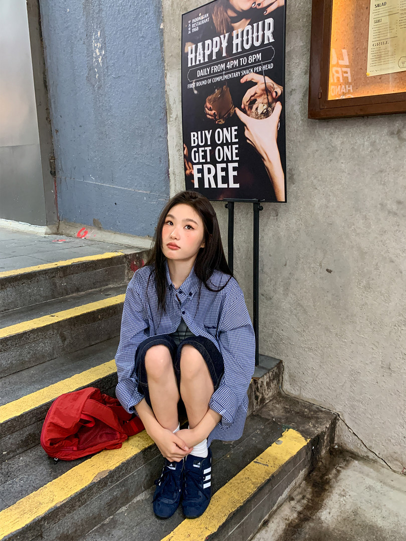 Woman wearing a blue checkered oversized shirt with sneakers, seated on outdoor steps