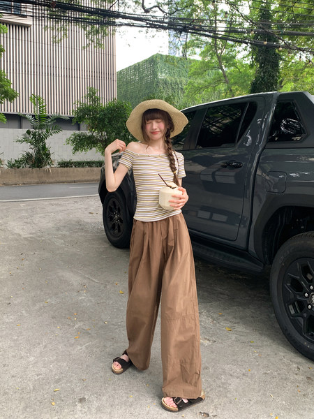 Woman wearing a striped off-shoulder top with brown wide-leg pants and a straw hat outdoors