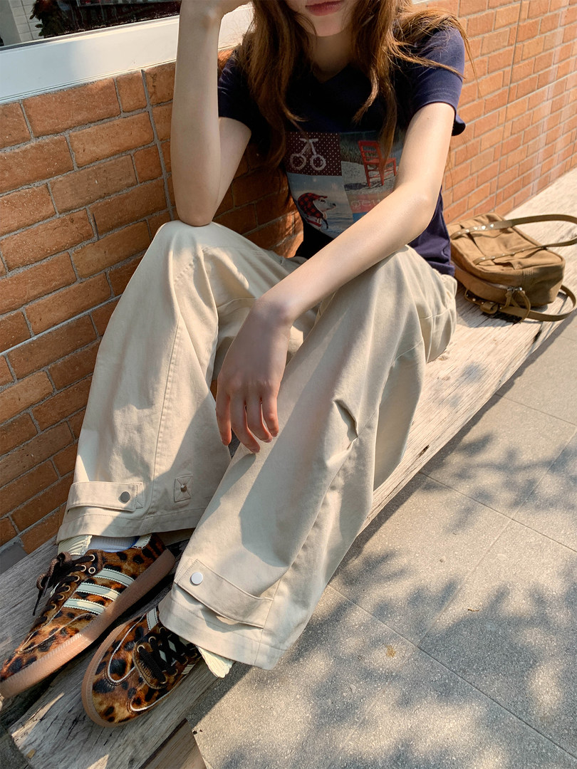 Model wearing a navy graphic T-shirt with loose beige wide-leg pants and leopard print sneakers outdoors