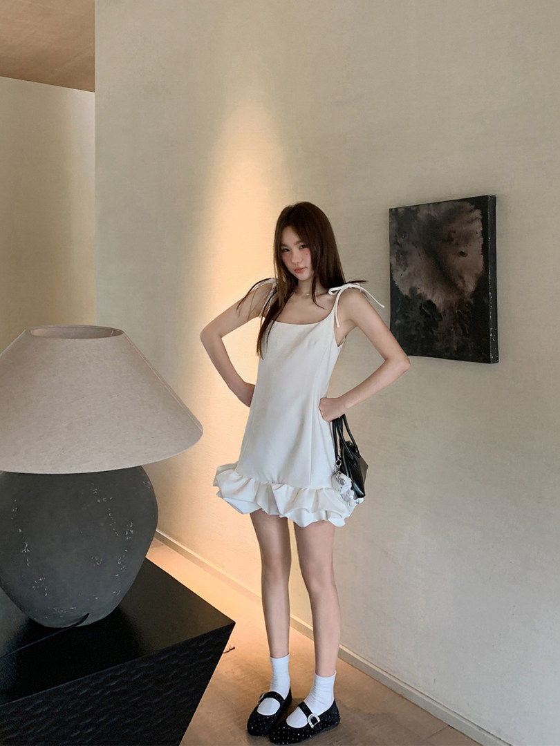 Model wearing a white sleeveless ruffle mini dress with black flats and a handbag