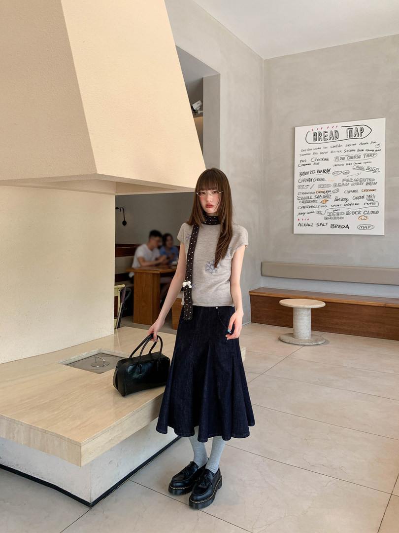 Woman wearing a gray top, dark skirt, scarf, and black bag in a cafe setting