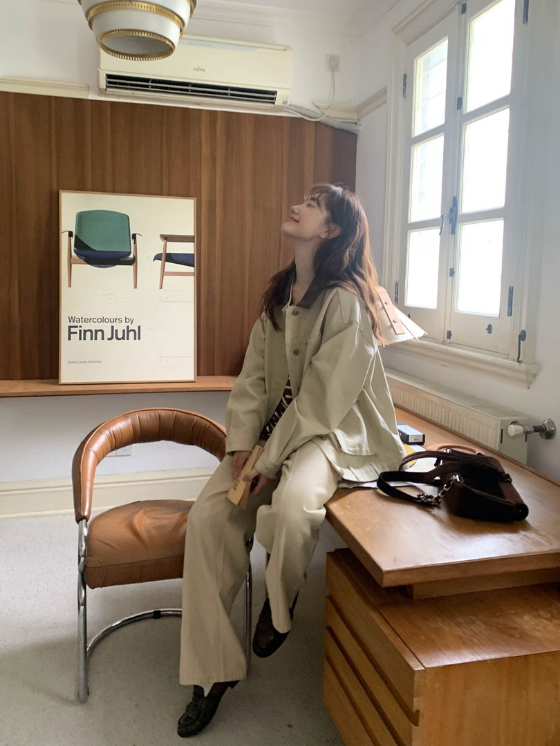 Woman wearing a beige oversized jacket and wide-leg pants seated indoors