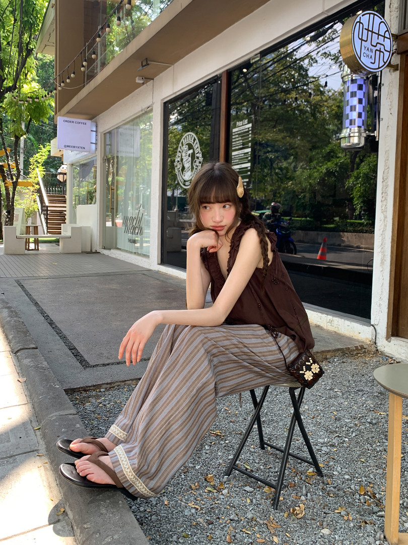 Woman wearing a brown sleeveless top with striped wide-leg pants and sandals seated outdoors at a cafe