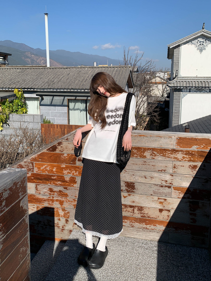 Woman wearing a white graphic T-shirt with a black polka dot skirt and black shoes outdoors