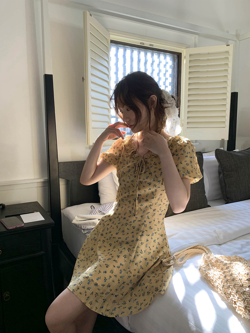 Woman wearing a yellow floral short-sleeve dress in a bedroom