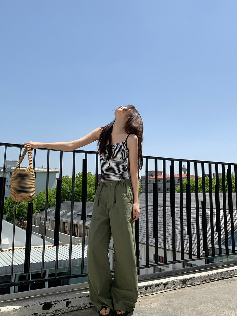 Woman wearing a striped tank top and olive wide-leg pants holding a woven bag outdoors