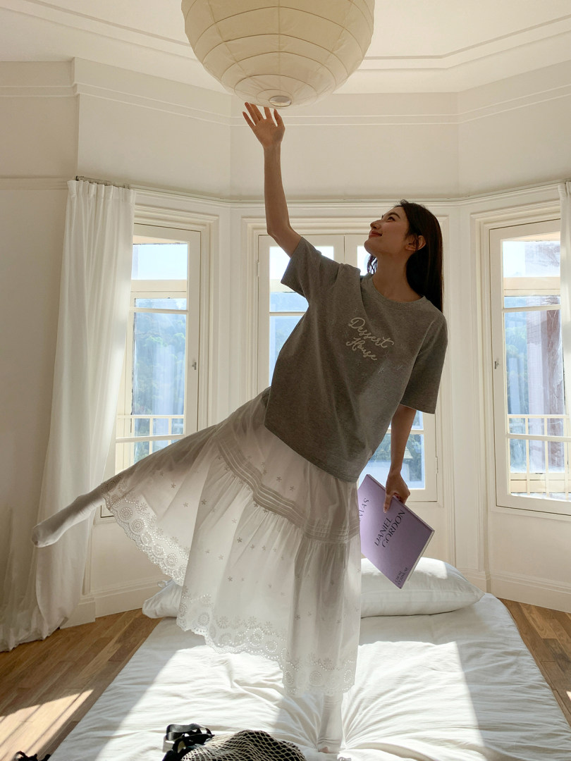 Woman modeling a grey graphic T-shirt and white lace skirt indoors