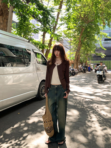 Model wearing a brown cardigan over a white top with wide-leg jeans and a woven tote bag on a street