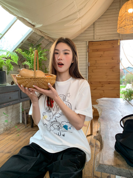 Woman wearing a white graphic T-shirt with black pants, holding a wicker basket indoors